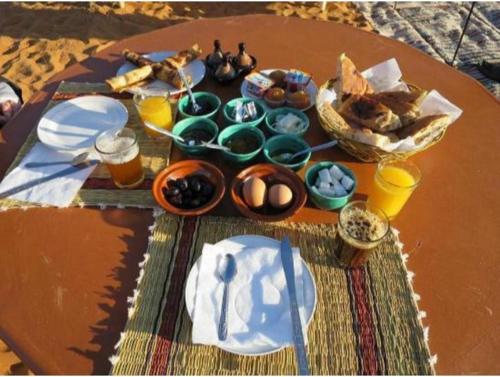 梅尔祖卡ERG MERZOUGA SAHARA CAMP的一张桌子上摆放着食物、盘子和饮料。