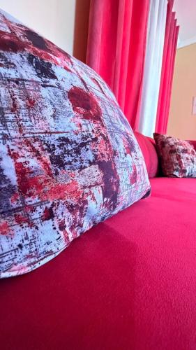 un cuscino su un letto con lenzuola rosse e tende rosse di LeGae Apartments a Gaborone
