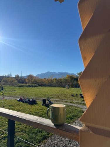 a cup of coffee sitting on a wooden railing looking out at a field at Cabana JagerBerg Rosenau in Râşnov