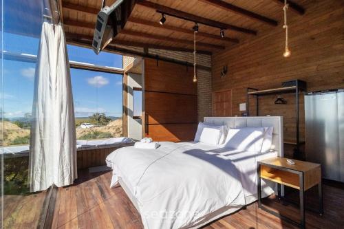 a bedroom with a white bed and a large window at Cabana c/ vista panorâmica e jacuzzi - VST026 in São Paulo dos Pinhais