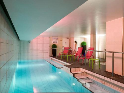 Una piscina con sillas rojas y una mujer al fondo. en Aparthotel Adagio Paris Centre Tour Eiffel, en París
