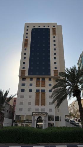 a tall building with a palm tree in front of it at فندق اصول الجوهرة بالعزيزية توصيل مجاني الى الحرم Asoul Al Jawhara Al Azizia Free Shuttle Service in Al ‘Azīzīyah