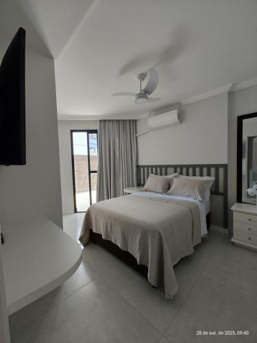 a white bedroom with a large bed and a window at Excelente apartamento com vaga garagem a 50 metros da orla da Praia do Morro Guarapari in Guarapari