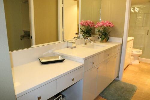 a bathroom with a sink and a mirror and pink flowers at Gulf and Bay Club- F105 in Siesta Key