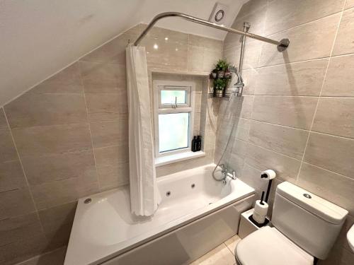 a bathroom with a tub and a toilet and a window at Cosy 3 Bedroom Flat, Hackney Central in London