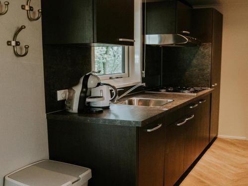 a kitchen with black cabinets and a sink and a window at Charming 5-Person Bee Lodge in the Woods in Balkbrug
