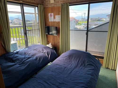 two beds in a room with a large window at 合同会社ゲストハウス縁 in Saijo