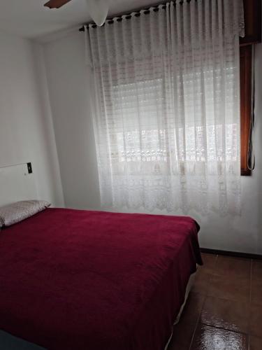 ein Schlafzimmer mit einem roten Bett und einem Fenster in der Unterkunft Aconchegante apto em Capao da Canoa in Capão da Canoa