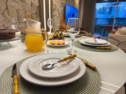 a table with plates and a glass of orange juice at MHV Milagres - Naluum G04, Casa em condomínio beira mar de alto padrão, a poucos metros da Capela dos Milagres in Passo de Camarajibe