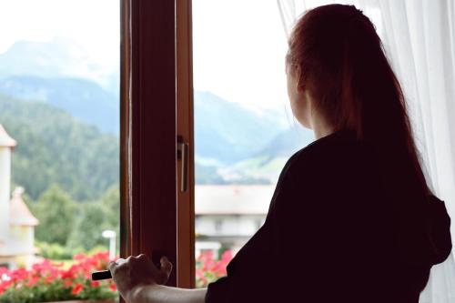 a woman looking out of a window holding a cigarette at Hotel & Suites Glück Auf in Mayrhofen