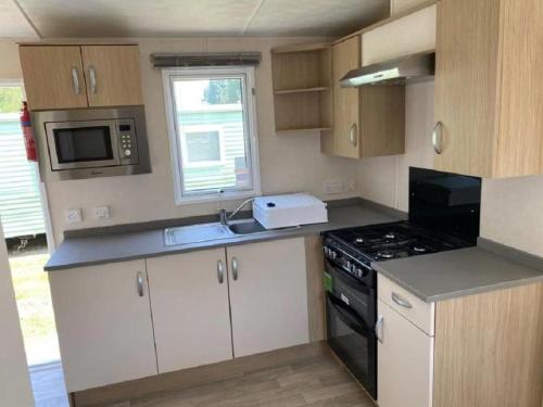 Una pequeña cocina con estufa y microondas. en Caravan With Front Decking At Coopers Beach Holiday Park Ref 49080Pa, en East Mersea