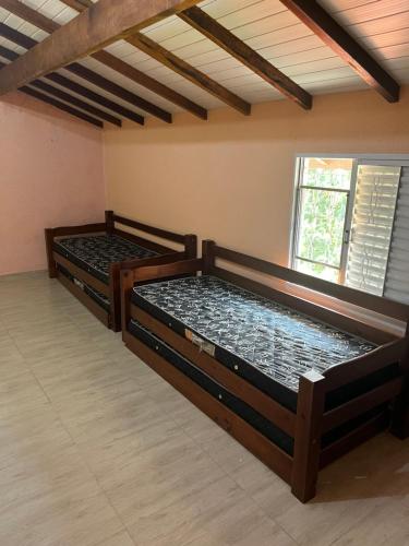 zwei Holzbetten in einem Zimmer mit Fenster in der Unterkunft Sarau's Beach House Boracéia in Boracéia