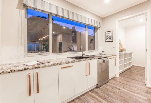 a kitchen with white cabinets and a large window at Hilltop Ocean Hideaway - Aotea Wellington in Porirua