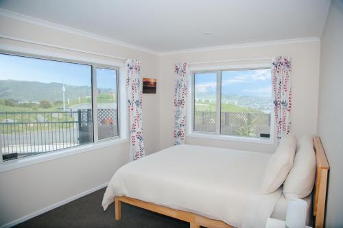 a white bedroom with a bed and two windows at Hilltop Ocean Hideaway - Aotea Wellington in Porirua