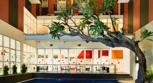 a building with a tree in front of a pool at Amaris Hotel Kupang in Klapalima