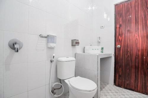 een witte badkamer met een toilet en een rode deur bij RedDoorz near Tugu Bandara Sulthan Thaha Jambi in Sultan Thaha Airport