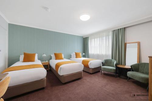 a hotel room with two beds and a chair at Mid City Motel Warrnambool in Warrnambool