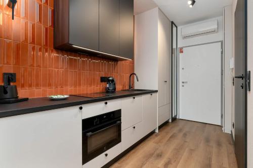 een keuken met witte kasten en een oranje tegelmuur bij Elegant Studio with Air Conditioning Pet Friendly by Noclegi Renters in Suchanino