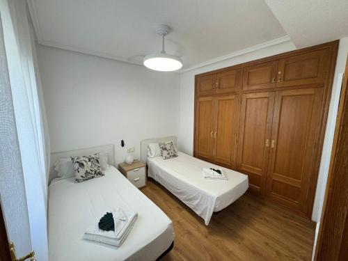 two beds in a small room with wooden cabinets at Homely Apartments Mar 3 in Torrevieja