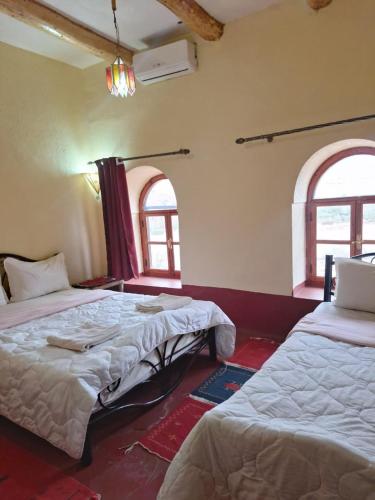 two beds in a room with two windows at La Fibule D'or in Aït Benhaddou