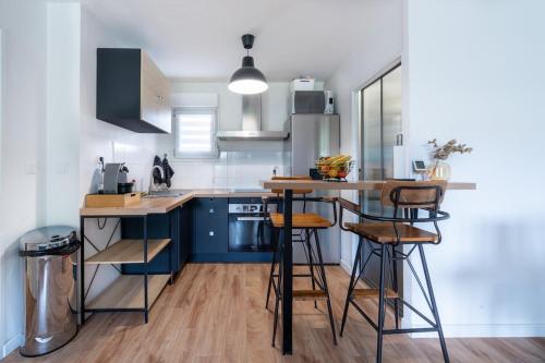 eine Küche mit blauen Schränken und einer Theke mit Stühlen in der Unterkunft Chez Adrien au Haillan Appt rez de chaussée jardin in Le Haillan