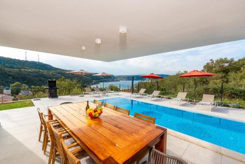 a dining area with a wooden table and a swimming pool at Villa Adria Blue in Bakarac