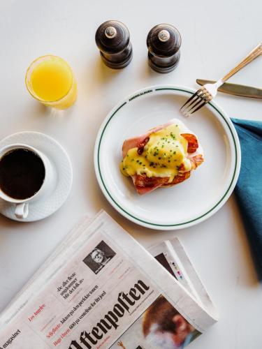 Un plato de comida sobre una mesa con un periódico y una taza de café. en Amerikalinjen, en Oslo