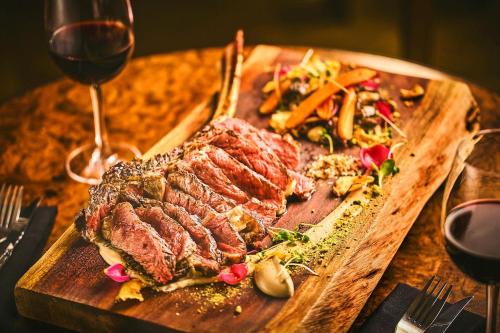 レイキャビクにあるアポテック ホテル レイキャビク バイ ケアホテルズのワイングラスの横のまな板の上にステーキが置かれている