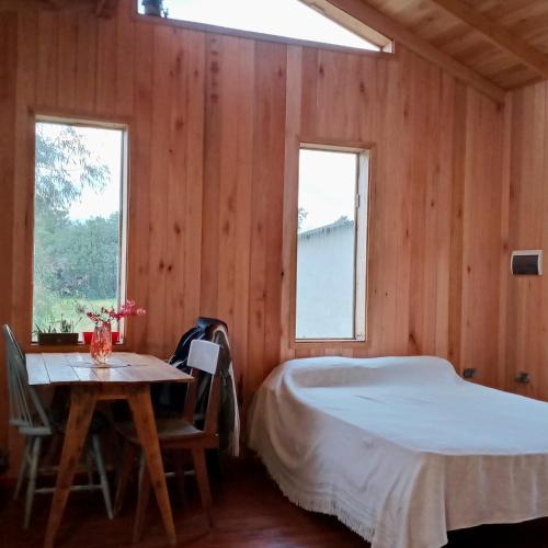 a bedroom with a bed and a table and windows at Cabaña entre molles in Punta Indio
