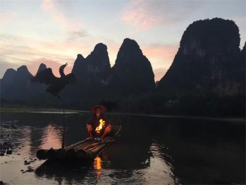 a man sitting around a fire in a boat in the water at Li-river Island Resort Xingping Yangshuo in Yangshuo