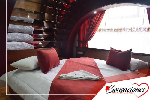 a bed with red and white pillows and a window at Motel Sensaciones in Latacunga