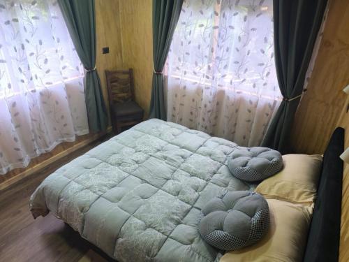 a bedroom with a bed and two windows with curtains at Cabaña La Casona in Chaitén