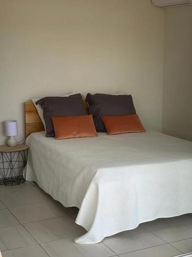 a white bed with orange and black pillows on it at Appartement spacieux avec vue sur la mer à Le Marin in Le Marin