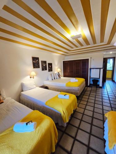 a room with three beds with yellow sheets at Pousada Gente Bonita Mirante in Búzios