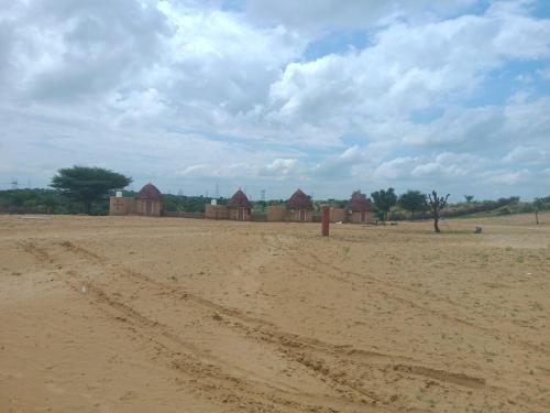 een onverharde weg met een groep gebouwen in de verte bij Raisar Desert Camp in Jāmb