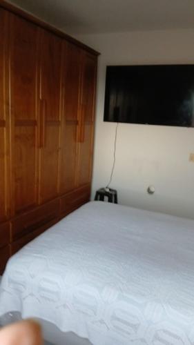 a bedroom with a white bed and a wooden cabinet at Apartamento coneglian in Itanhaém