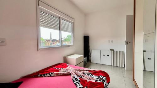 a bedroom with a red bed and a window at Casa pertinho do mar in Capão da Canoa