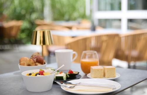 a table with a plate of food and a glass of orange juice at Leonardo Hotel Muenchen City West in Munich