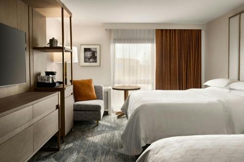 a hotel room with two beds and a tv and a chair at Madison Marriott South in Madison