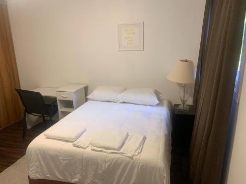een slaapkamer met een bed met witte lakens en een bureau bij Napaeno's Place - Home Away from Home in Kingston