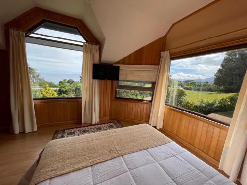 a bedroom with a bed and two large windows at Beautiful Plot Lake and Volcano View in Puerto Varas