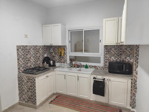 a kitchen with white cabinets and a sink and a microwave at immeuble brini in Kairouan