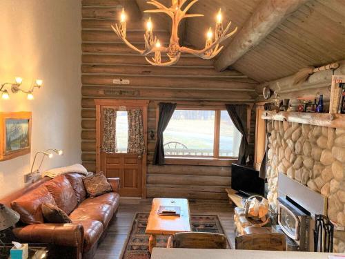 a living room with a leather couch and a chandelier at Rocky Mountains Nature Escape: Amazing Log Cabin with a Hot Tub in Darby, MT in Peaks and Pines Park