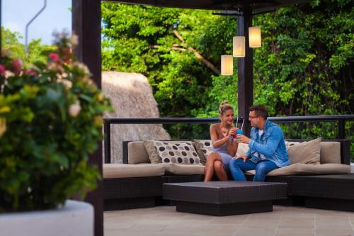 a man and woman sitting on a bench looking at their cell phone at The Reef Playacar Beach Resort & Spa-Optional All Inclusive in Playa del Carmen