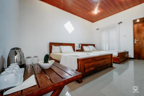 a bedroom with two beds and a wooden table with a kitchen at Lotus Udawalawe in Udawalawe