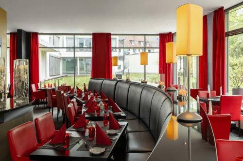 un comedor con sillas rojas, mesas y ventanas en Ramada by Wyndham Essen, en Essen