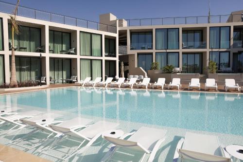 una piscina con sedie a sdraio bianche di fronte a un edificio di Inanna Resort a Batroûn