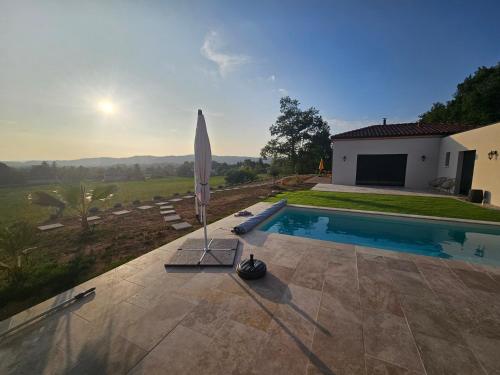 une piscine avec un parasol à côté d'une maison dans l'établissement La Panurama, à Prayssac