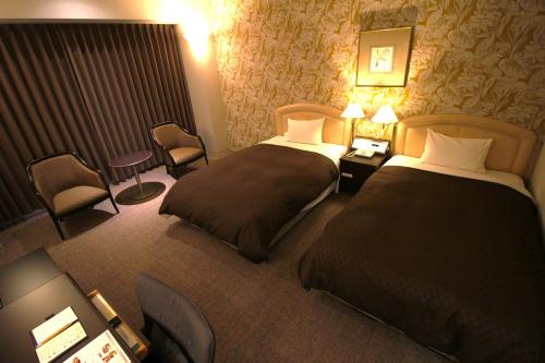 a hotel room with two beds and a chair at Rembrandt Hotel Oita in Oita