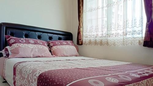 a bed with pink and white pillows and a window at COZY 2BR Pinewood Apt Jatinagor in Cilimus 2